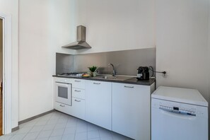 A compact kitchen with a stove, sink, and dishwasher, white cabinets, and a stainless steel range hood. - iFlat | Classic roman palazzo Fons Trevi A15 (Rome)