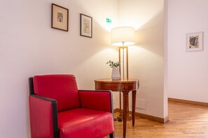 A red chair, a lamp, and framed artwork on a wall in a room with wooden flooring. - iFlat | Classic roman palazzo Fons Trevi A15 (Rome)