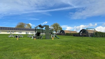 A playground with climbing structures and swings, a picnic table, and a building with a sloped roof in the background.