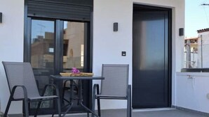 A balcony with two chairs and a table, a sliding door, and a window with a view of buildings.