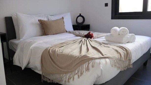 A neatly made bed with a beige throw blanket, white pillows, and a small bedside table with a decorative item.