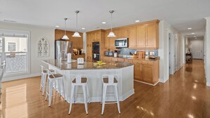 Una cocina moderna con armarios de madera, una isla central con taburetes de bar, electrodomésticos de acero inoxidable e iluminación colgante.