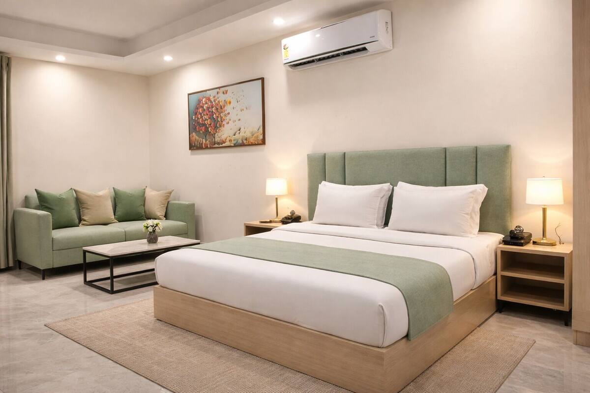 A hotel room with a bed, a sofa, a coffee table, and an air conditioning unit.
