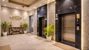 A modern lobby with two elevators, a reception desk, and potted plants. - OPO Premier MARVEL (Jaipur)