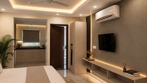 A modern bedroom with a bed, ceiling fan, air conditioning unit, TV, and a kitchen area in the background. - OPO Premier MARVEL (Jaipur)
