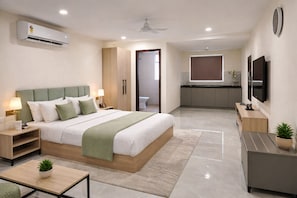 Una habitación de hotel moderna con cama, mesitas de noche, escritorio, televisor y kitchenette.