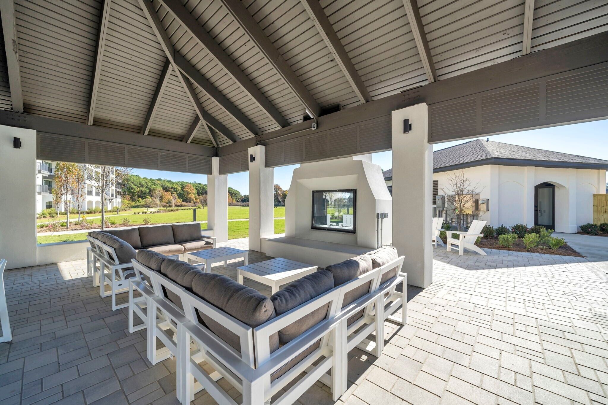 Un patio extérieur couvert, agrémenté de mobilier blanc, offrant une vue sur un paysage verdoyant et avec un bâtiment visible à l’arrière-plan.