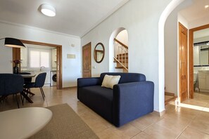 Un salon avec un canapé, une table à manger et des chaises. Un escalier mène à l’étage supérieur.