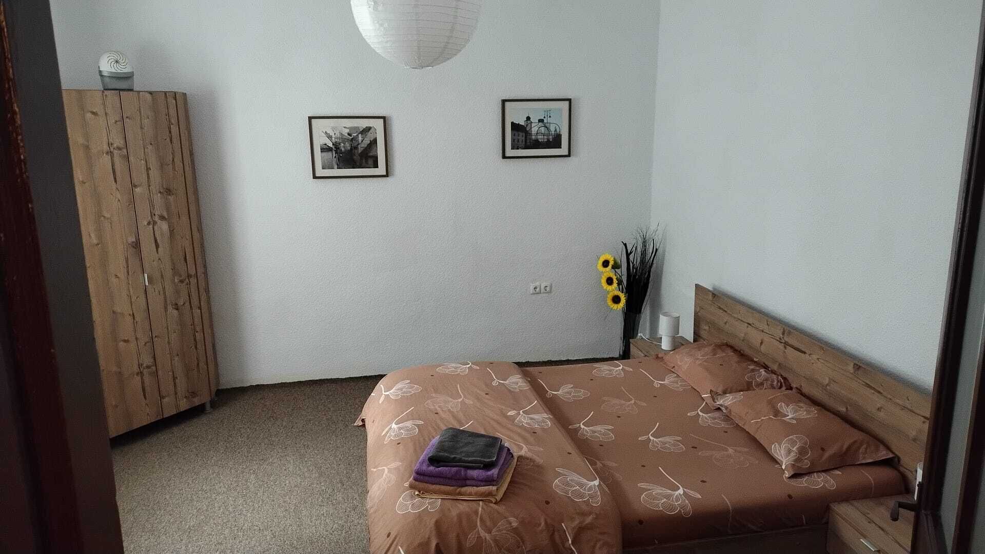 Une chambre à coucher avec un lit, une armoire en bois, deux tableaux encadrés au mur et un vase rempli de tournesols.