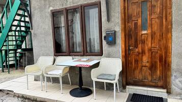 Um quarto com porta de madeira, janela com cortinas, uma mesa com cadeiras e um lance de escadas verdes.