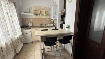 Een compacte keuken met een centraal eiland, barstoelen, een magnetron en een klok aan de muur.