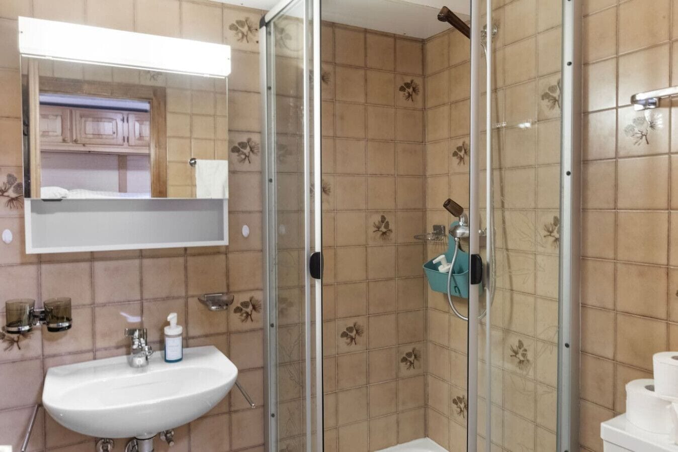 Et badeværelse med brusekabine i glas, vask med spejl og toilet.