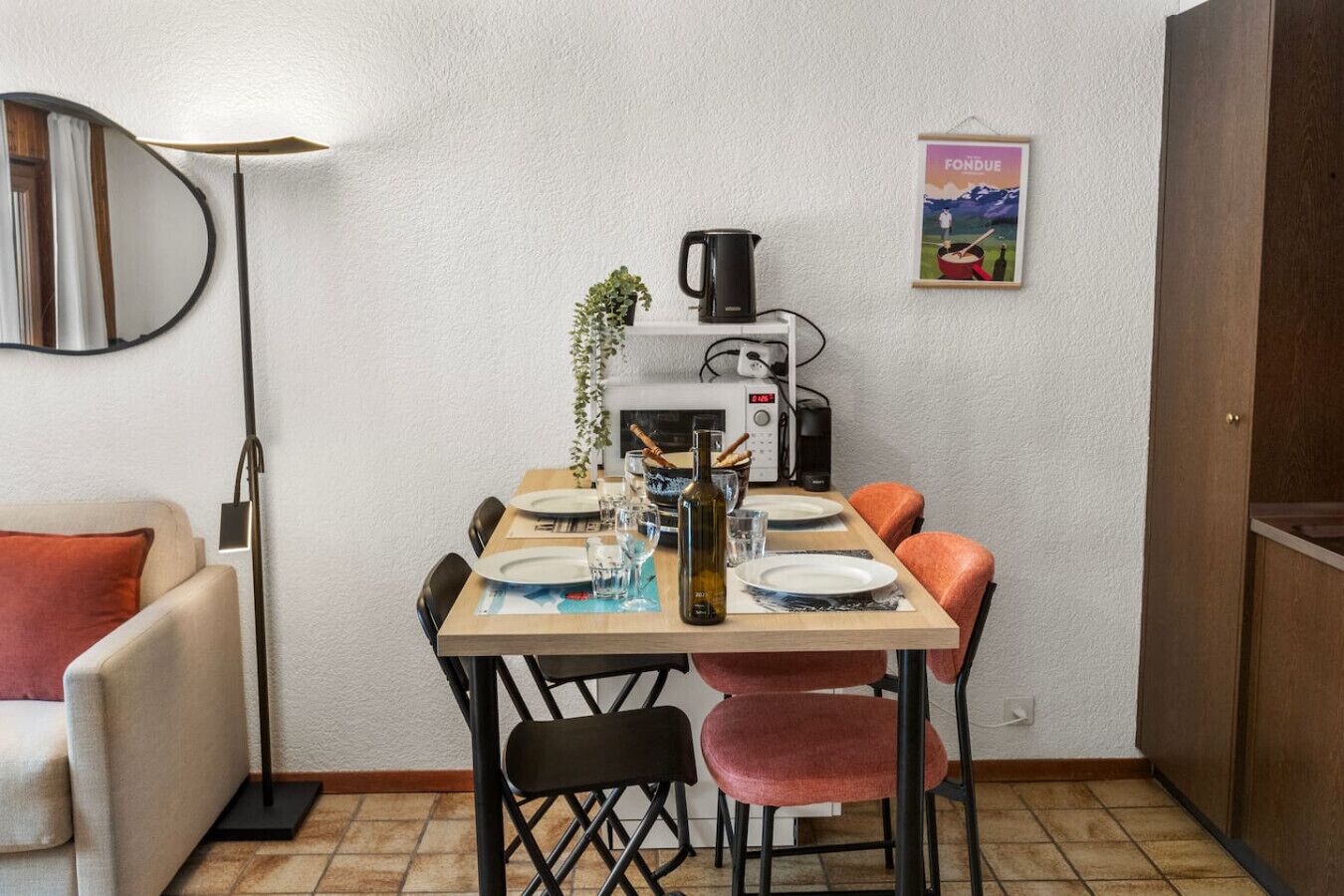 A compact kitchen with a dining table set for two, a microwave, a kettle, and a framed picture on the wall.