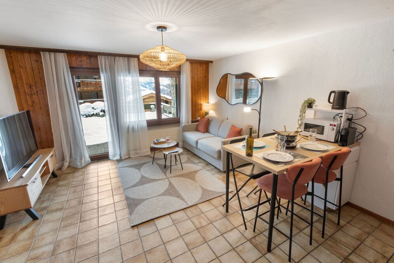Een functionele woonruimte met een bank, eettafel, stoelen, een televisie en een keukenhoek met een magnetron.