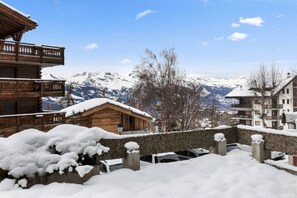 Un chalet in legno con un balcone, un muro in pietra e vista sulle montagne innevate.