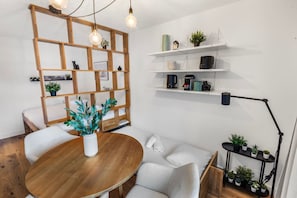 A modern living room with a wooden dining table, a sofa, a coffee table, and a bookshelf with plants. - Élégant studio à proximité des pistes et des bains (Leukerbad)