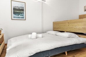 A neatly made bed with white bedding and pillows, a wooden headboard, a bedside table with a plant, and a framed picture on the wall. - Charmant studio, proche des bains et de la nature (Leukerbad)