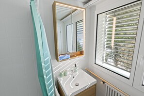 A bathroom with a large mirror, a window with blinds, a sink, and a towel rack. - Charmant studio, proche des bains et de la nature (Leukerbad)