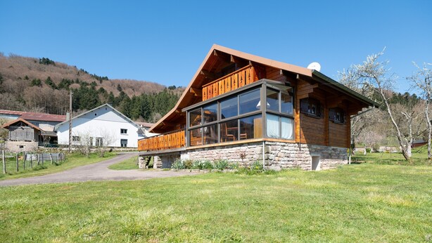 Una cabaña de madera con base de piedra, ventanas grandes y un balcón.