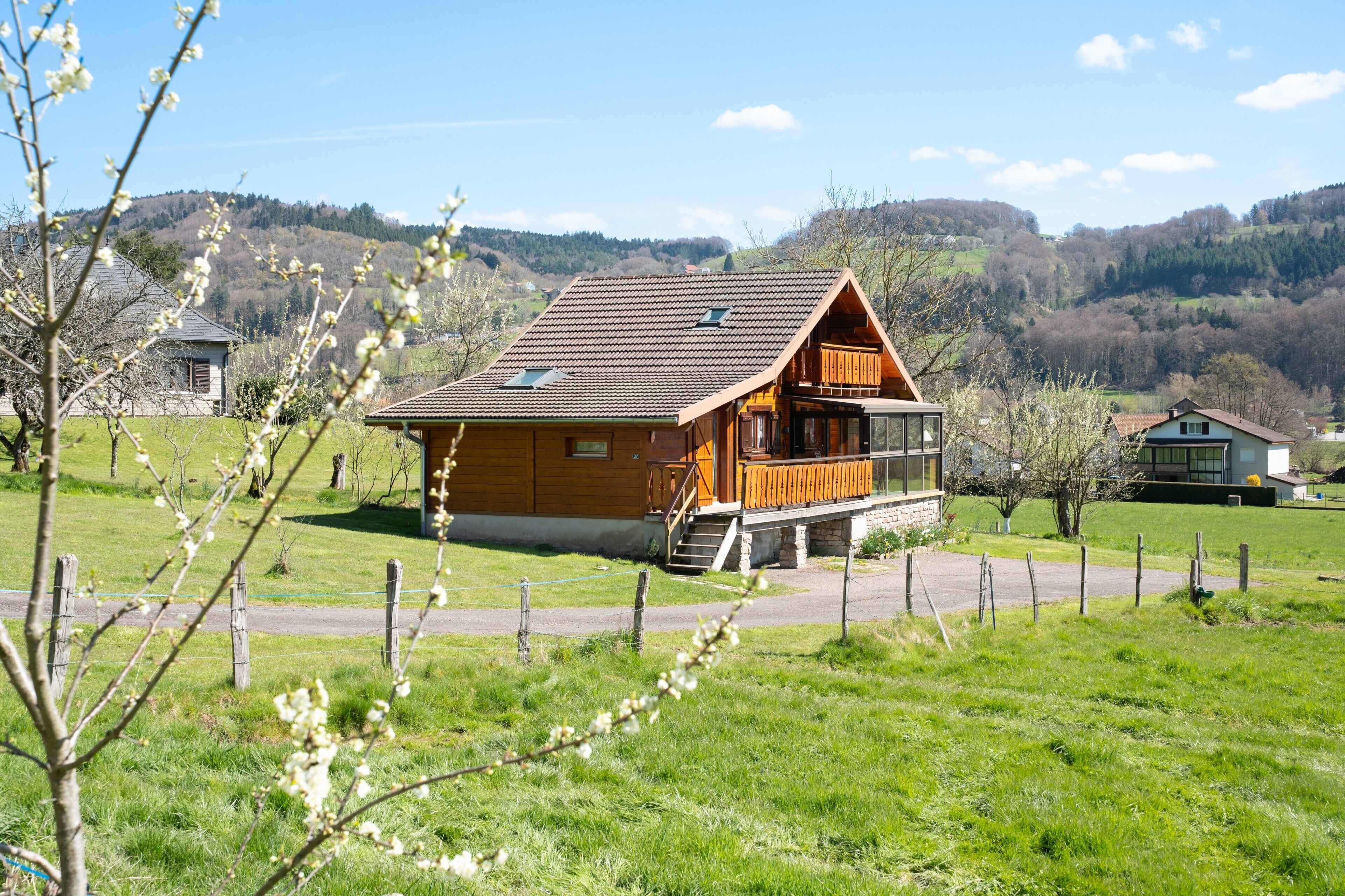 Een houten chalet met een balkon, gelegen in een groen veld met een berg op de achtergrond.