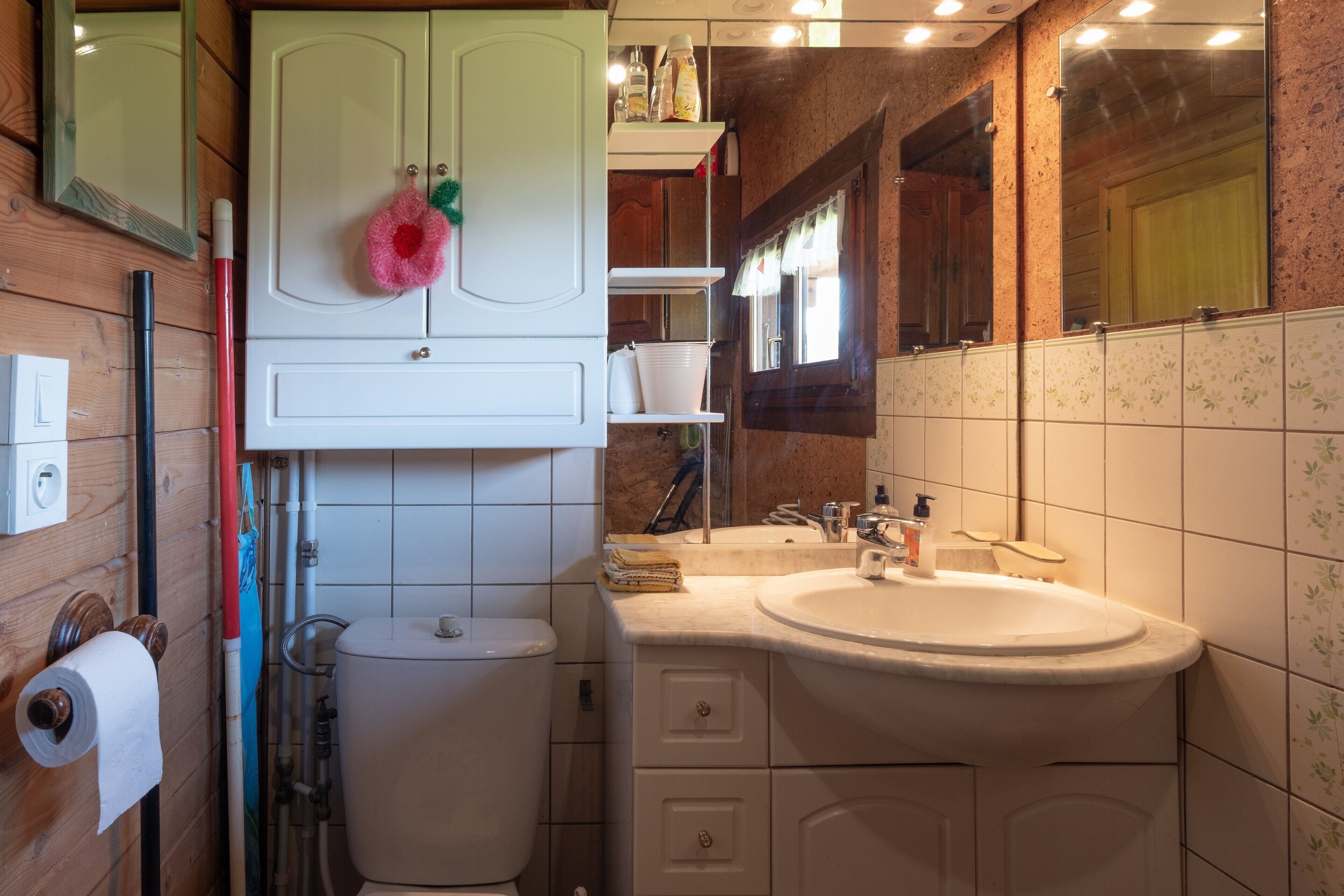 A bathroom with a toilet, sink, mirror, and wooden cabinets.