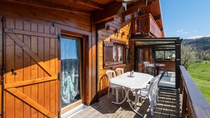 Una cabaña de madera con un porche, una mesa de comedor, sillas y vistas al paisaje.