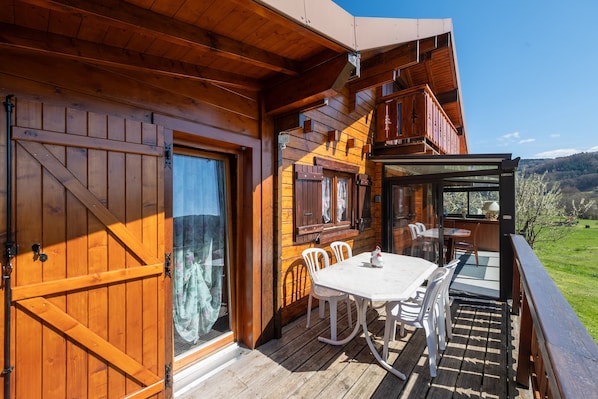Una cabaña de madera con un porche, una mesa de comedor, sillas y vistas al paisaje.