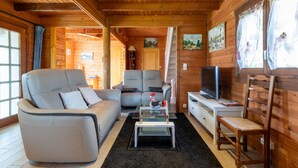 Interior de una cabaña de madera con sofá, sillón, televisión y una mesita.
