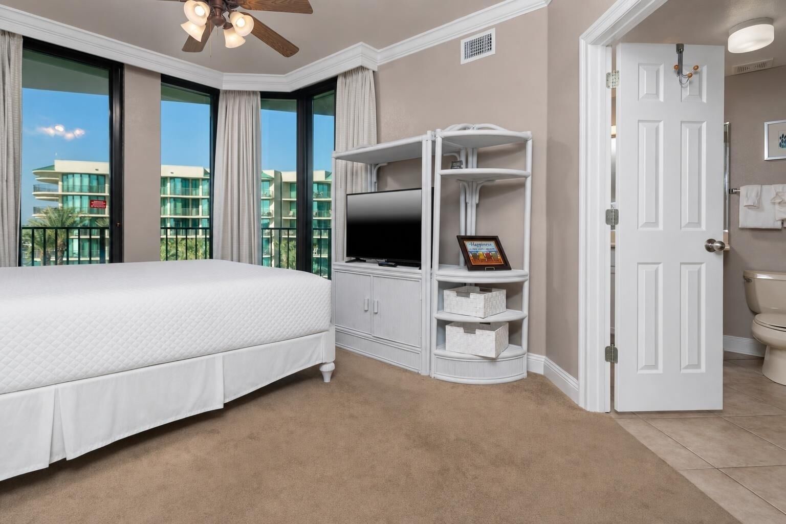 A hotel room with a bed, a TV, a white storage unit, and a door leading to the bathroom.