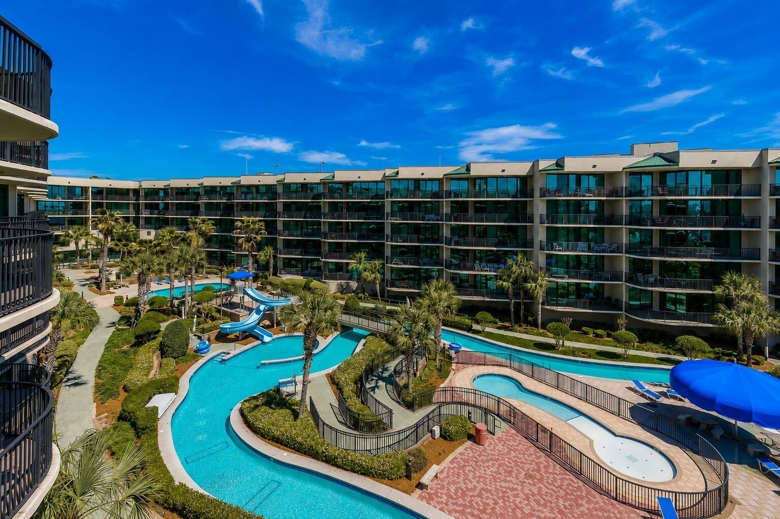 A hotel with multiple floors, a pool area with a water slide, and palm trees.