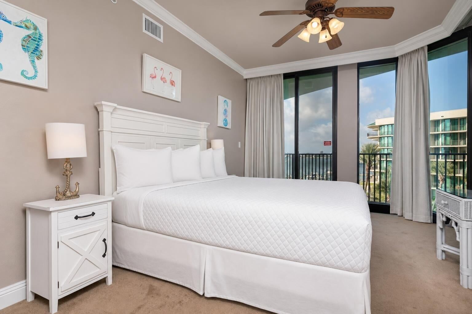 Habitación de hotel con cama, mesita de noche, ventilador de techo y vista a la ciudad.