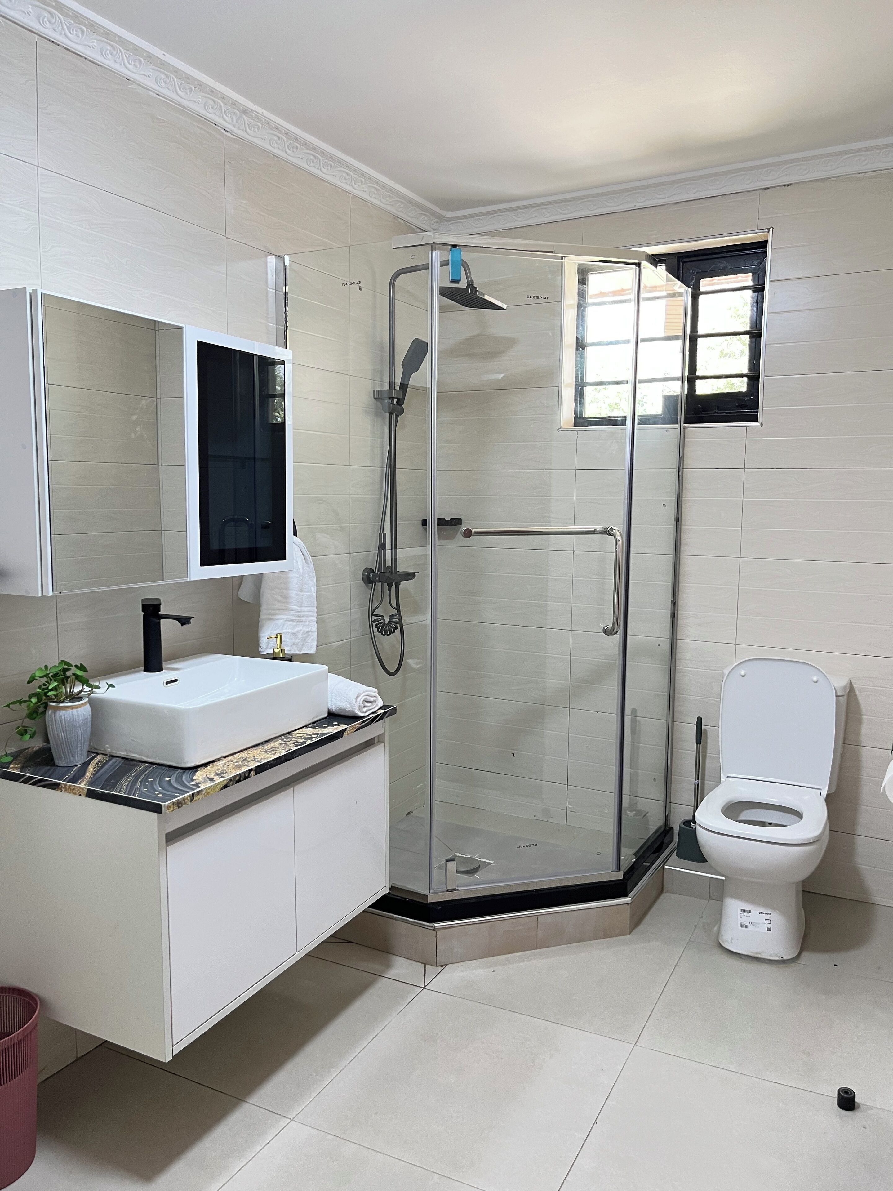 A modern bathroom with a glass-enclosed shower, a white sink with a marble countertop, and a toilet.