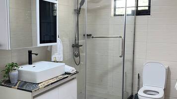 A modern bathroom with a glass-enclosed shower, a white sink with a marble countertop, and a toilet.