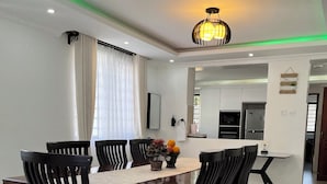 A dining area with a wooden table and chairs, a vase with flowers, and a kitchen in the background.