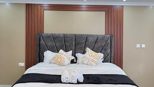 A modern hotel room with a large bed, a headboard with vertical wooden panels, and a ceiling with recessed lighting.