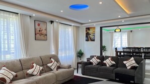A living room with two sofas, a dining table, and a large window with curtains.