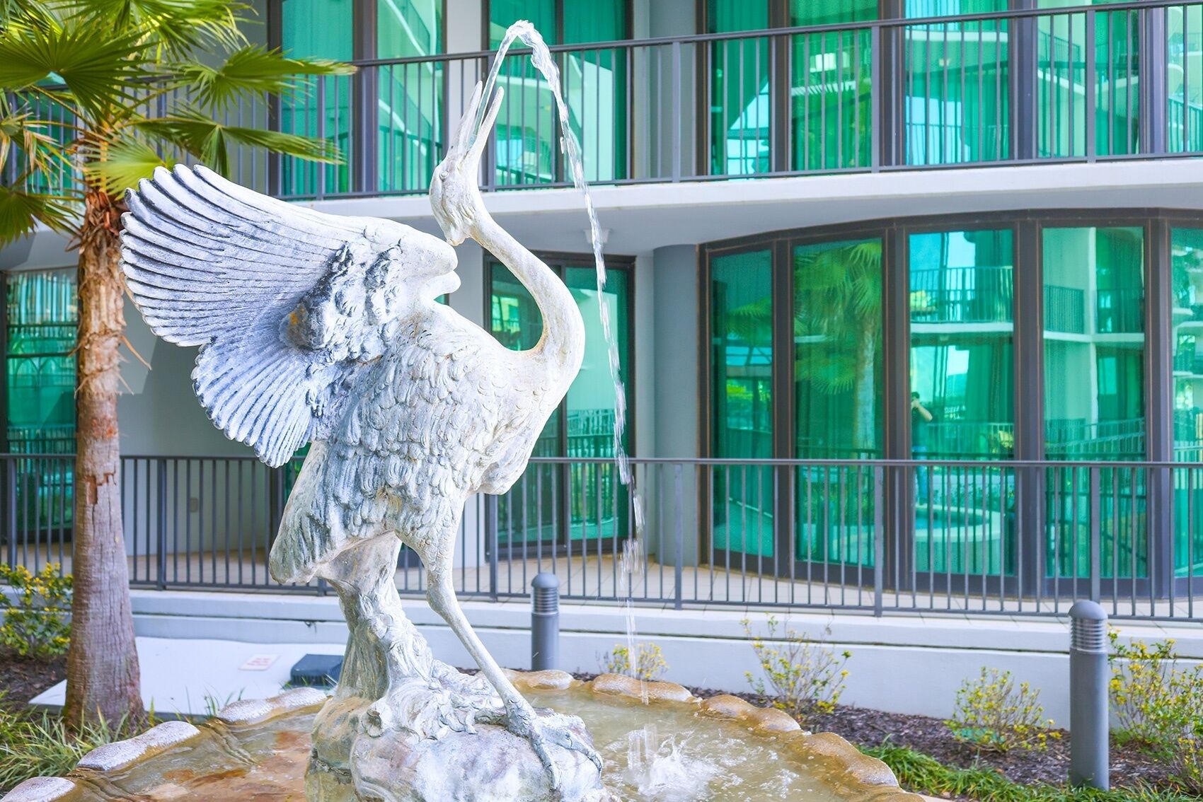 Een beeld van een vogel met uitgestrekte vleugels in een fontein, voor een modern gebouw met grote ramen.