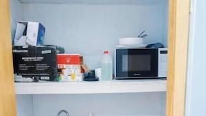 Un baño pequeño con un lavabo, un microondas y un estante con artículos de aseo.