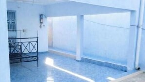 Una habitación amplia con piso de baldosas azules, estructura de cama metálica y techo blanco con tuberías expuestas.