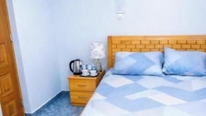 Un dormitorio con una cama de madera, una mesita de noche, un tapete azul y suelo de mármol.