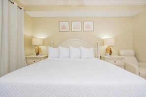 A hotel room with a large bed, two bedside tables with lamps, a chair, and three framed pictures on the wall. - Phoenix On The Bay 1206 2 Bedroom Condo (Orange Beach)
