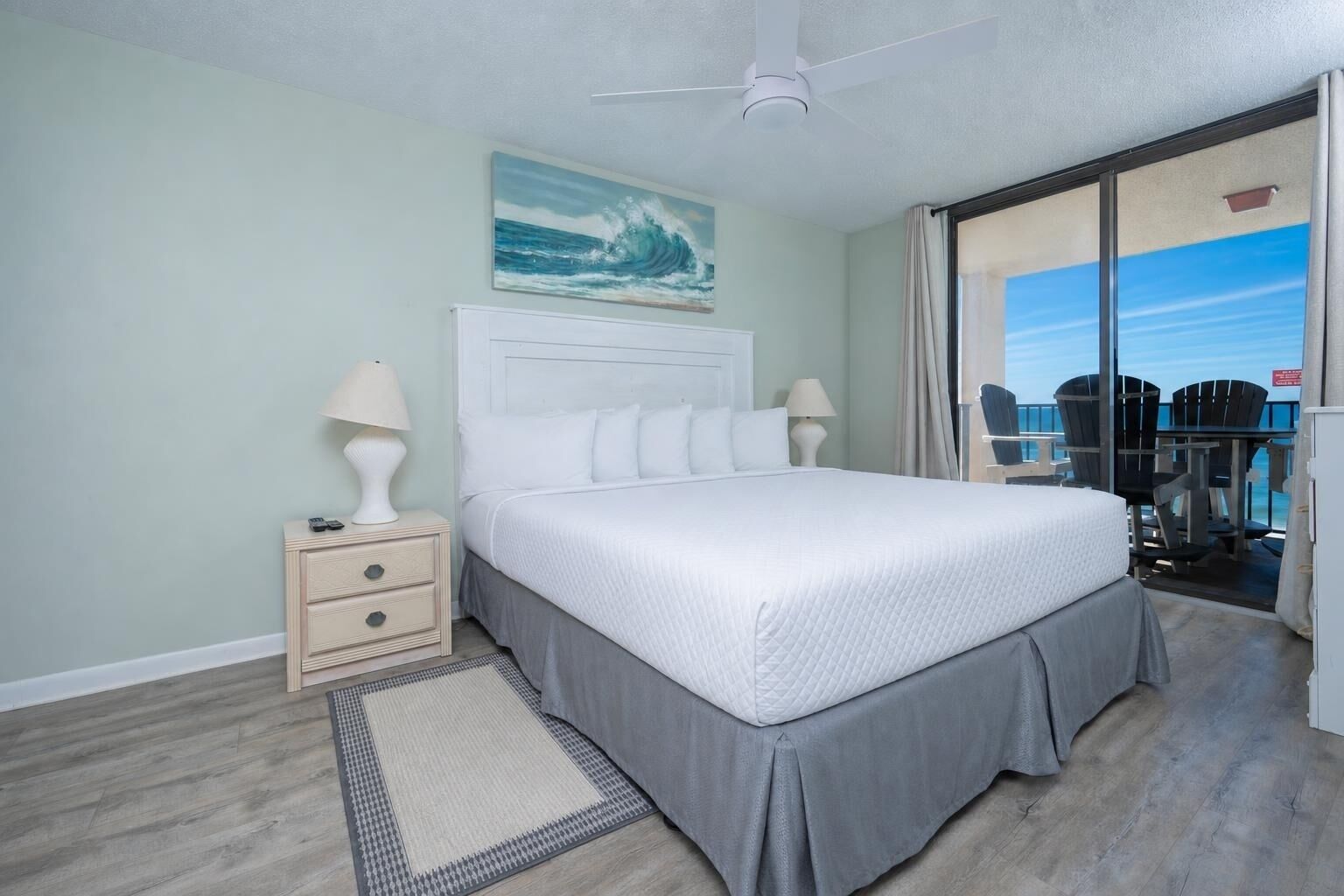 A bedroom with a bed, nightstands, a rug, and a view of the ocean through a sliding door.