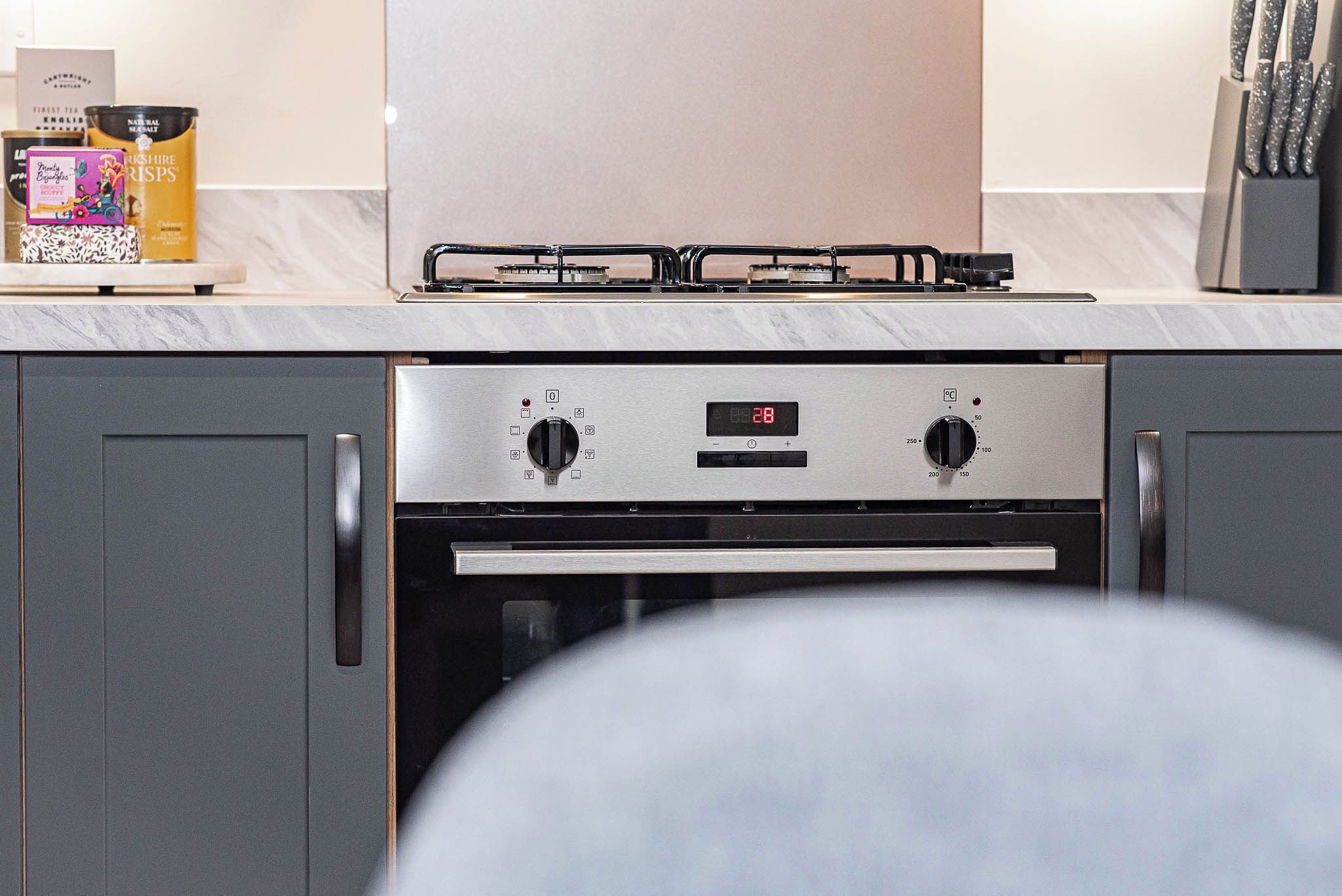 A kitchen with a digital clock, stainless steel appliances, and a marble countertop.