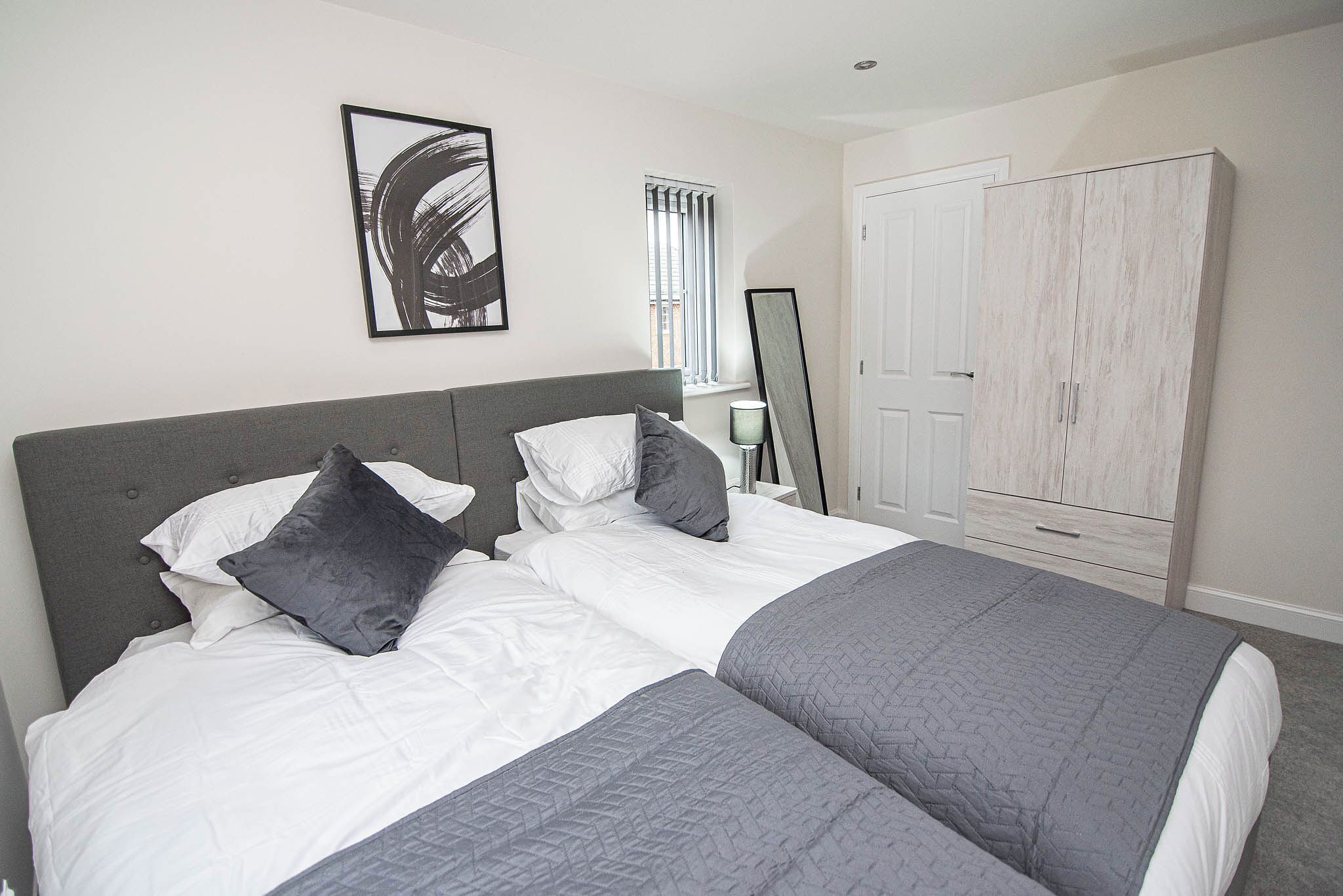 A bedroom with a bed, a wardrobe, a mirror, and a painting on the wall.
