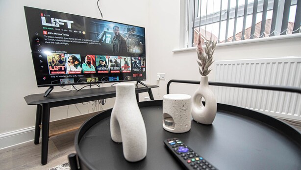 Un téléviseur à écran plat posé sur un meuble, une télécommande et deux vases décoratifs sur une table ronde.