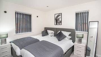 Une chambre à coucher avec un lit double, deux tables de chevet, un miroir et une fenêtre avec des stores.