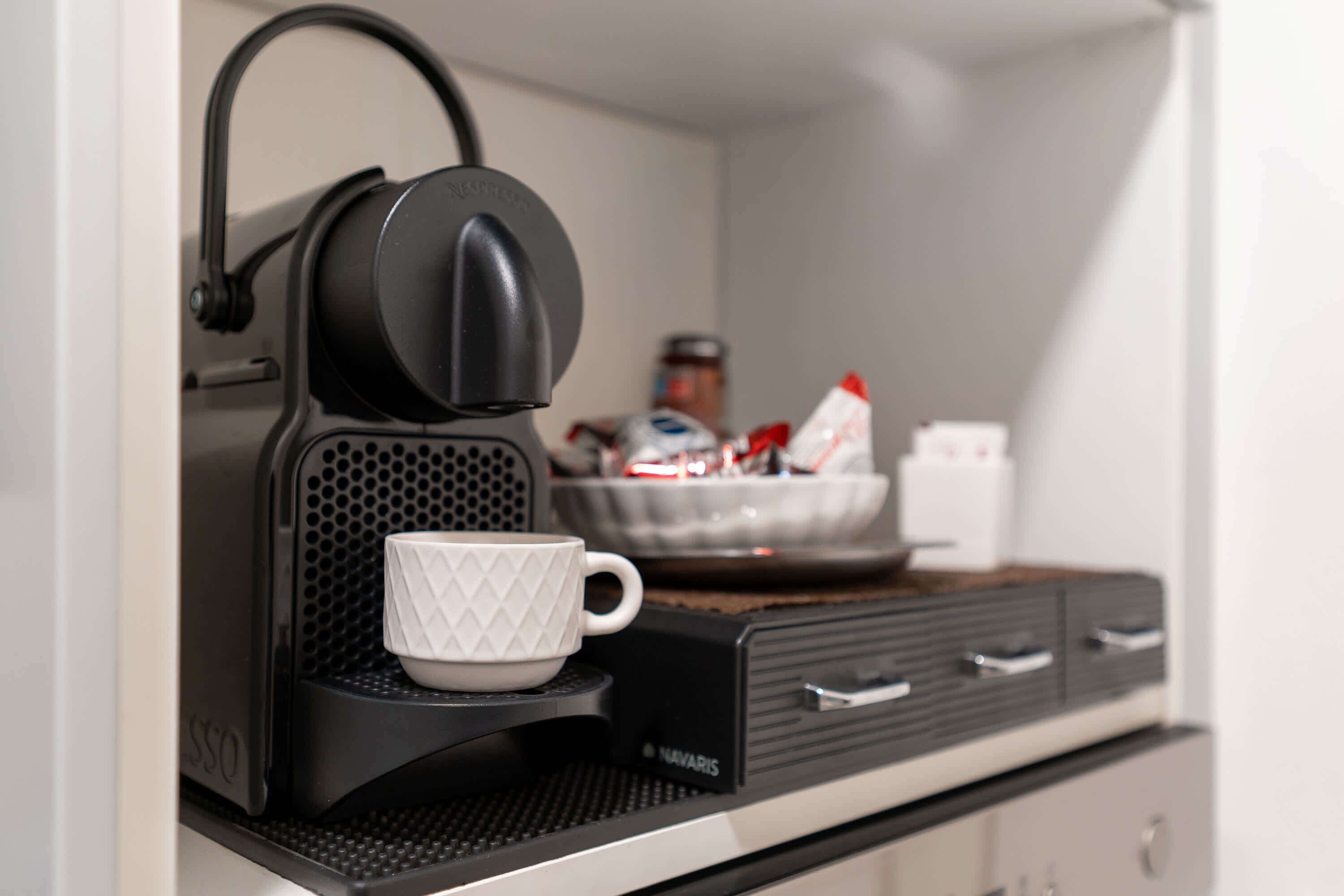 Eine Kaffeemaschine mit Tasse auf einem Tablett, eine Schüssel und ein Schrank mit Schubladen.