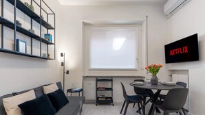 Een moderne woonruimte met een bank, eettafel, stoelen, een televisie en een boekenkast.