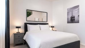 Een keurig opgemaakt slaapkamer met een bed, nachtkastjes, een spiegel en een ingelijst schilderij aan de muur.