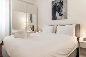 Hotellihuone, jossa on suuri sänky, yöpöytä, peili ja maalaus, jossa on kuvattuna hevonen.